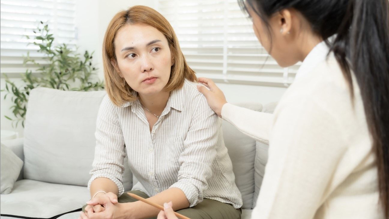 Female asian psychologist comforting concerned single mother during counseling session in therapy room offering mental health support