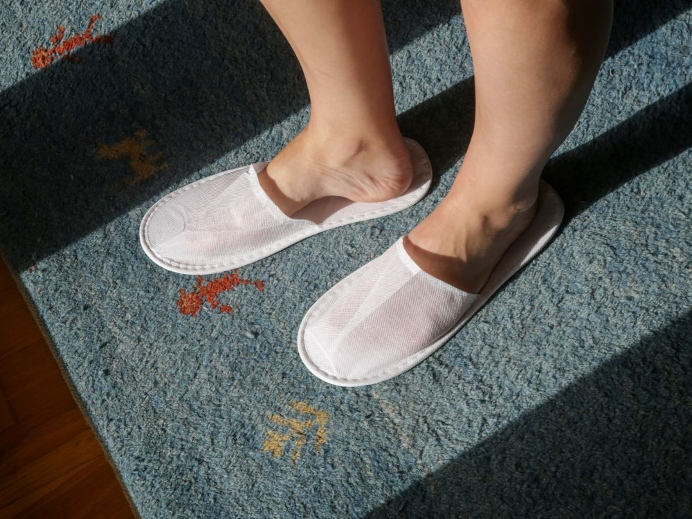 A traveller wears slippers on a carpeted hotel room floor