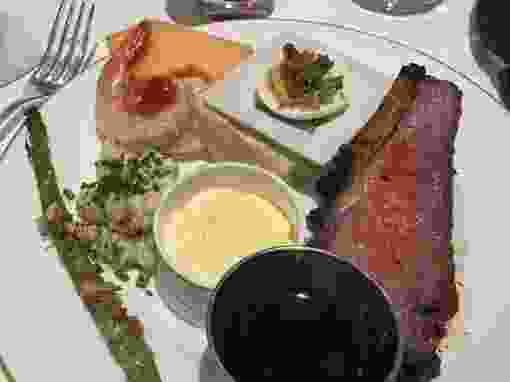 Shrimp, asparagus, melon, deviled egg, prime rib and jus on plate
