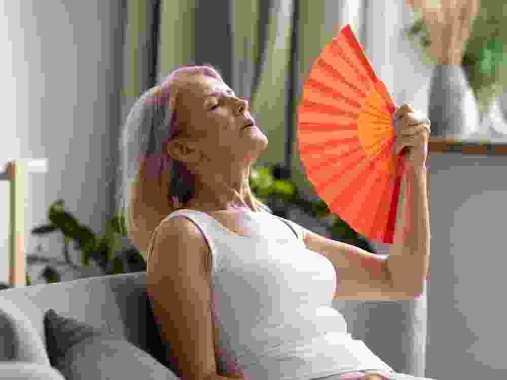 Stressed old woman waving fan suffer from overheating at home