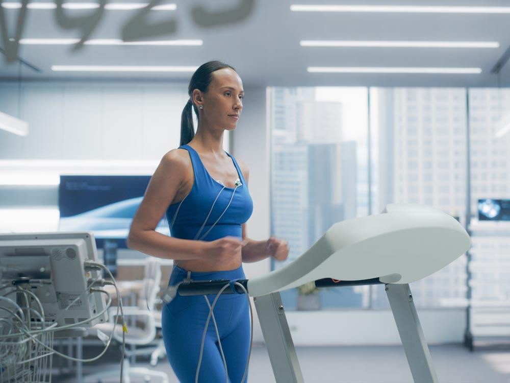 Female Athlete in Blue Workout Gear Runs on a Treadmill in a Modern Medical Lab, Monitored by Sensors for Advanced Fitness and Health Assessment Program