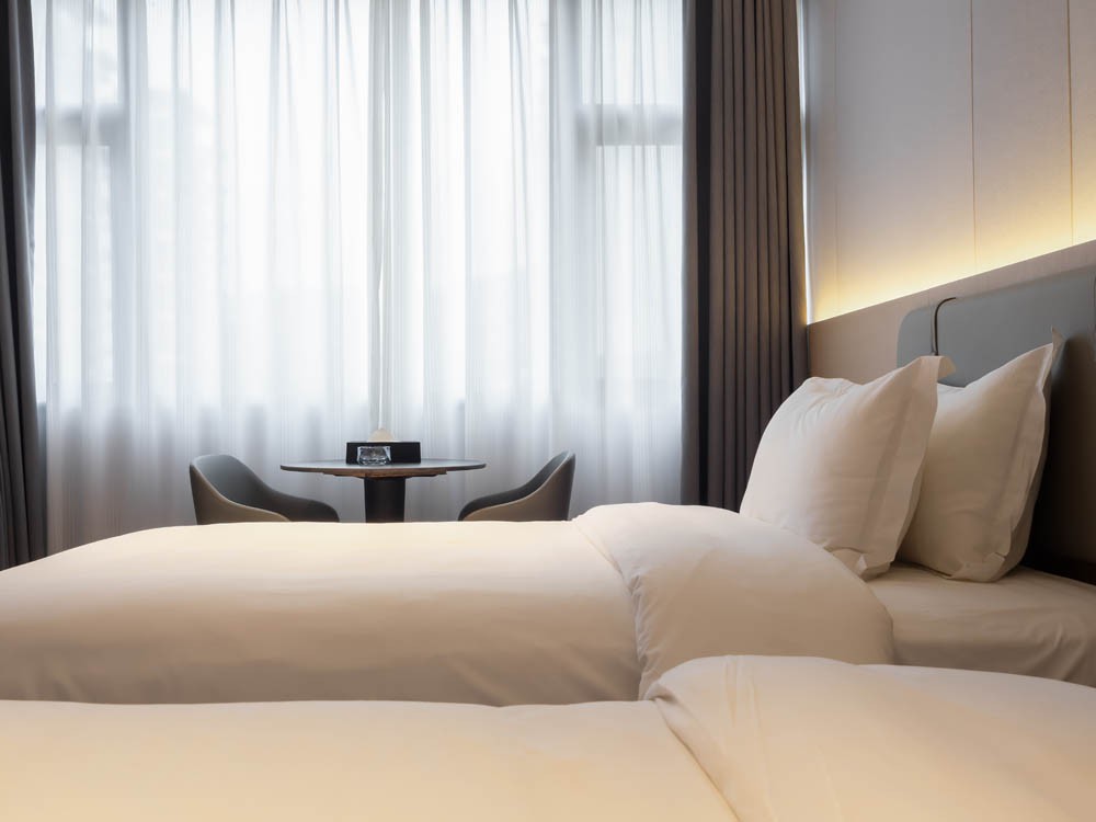 Clean hotel bedroom background with neatly arranged white bedding, soft lighting, and peaceful atmosphere, ideal for concepts of relaxation, comfort, hospitality, and premium travel accommodation.