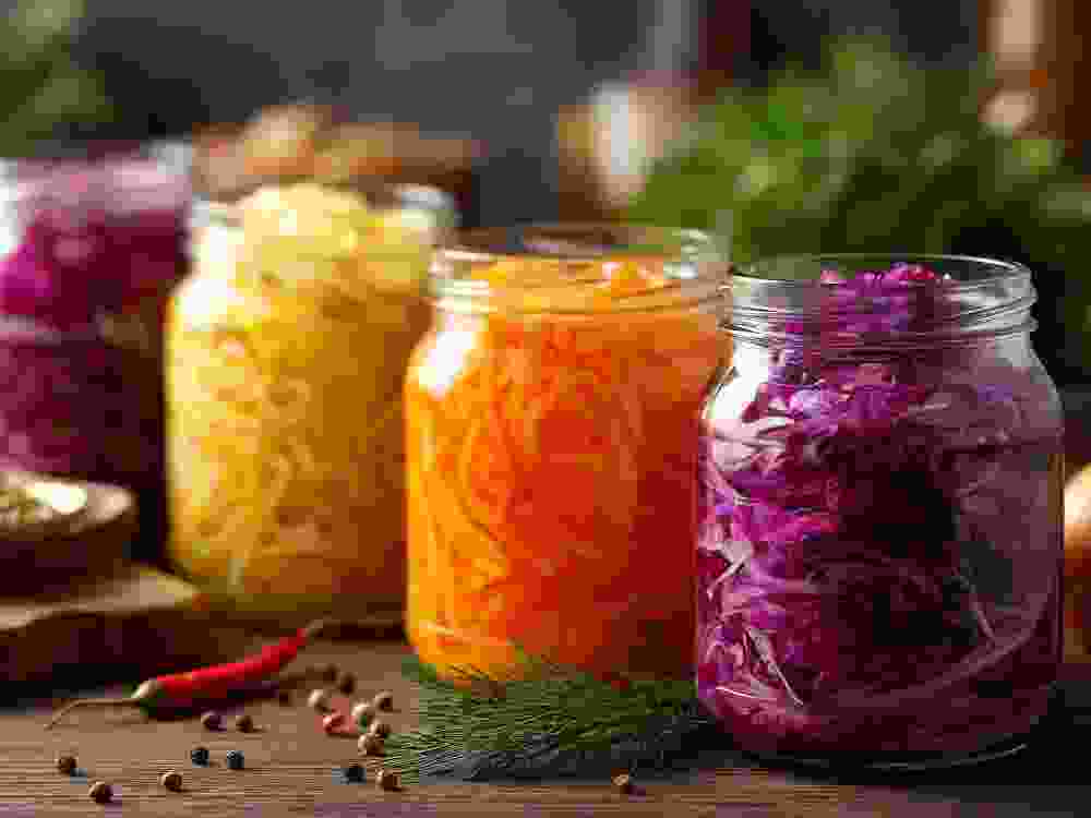Rustic kitchen scene with homemade fermented vegetables jars, preserved foods including various pickled vegetables displayed, wooden countertop with fresh ingredients and spices
