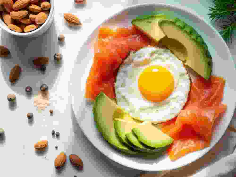 Balanced breakfast plate with fried egg salmon avocado and almonds. Healthy meal offers protein healthy fats and vitamins. Morning food presented on white plate with natural light.