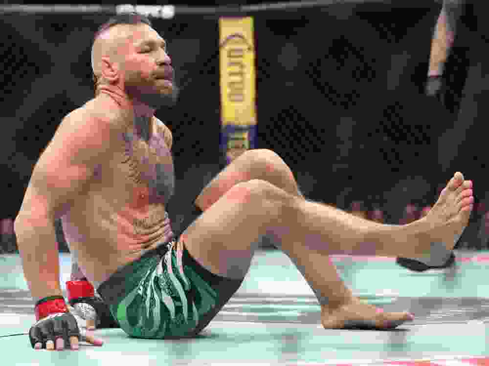 Conor McGregor falls after sustaining an injury on a kick in the first around against Max Holloway in their welterweight bout during UFC 329.