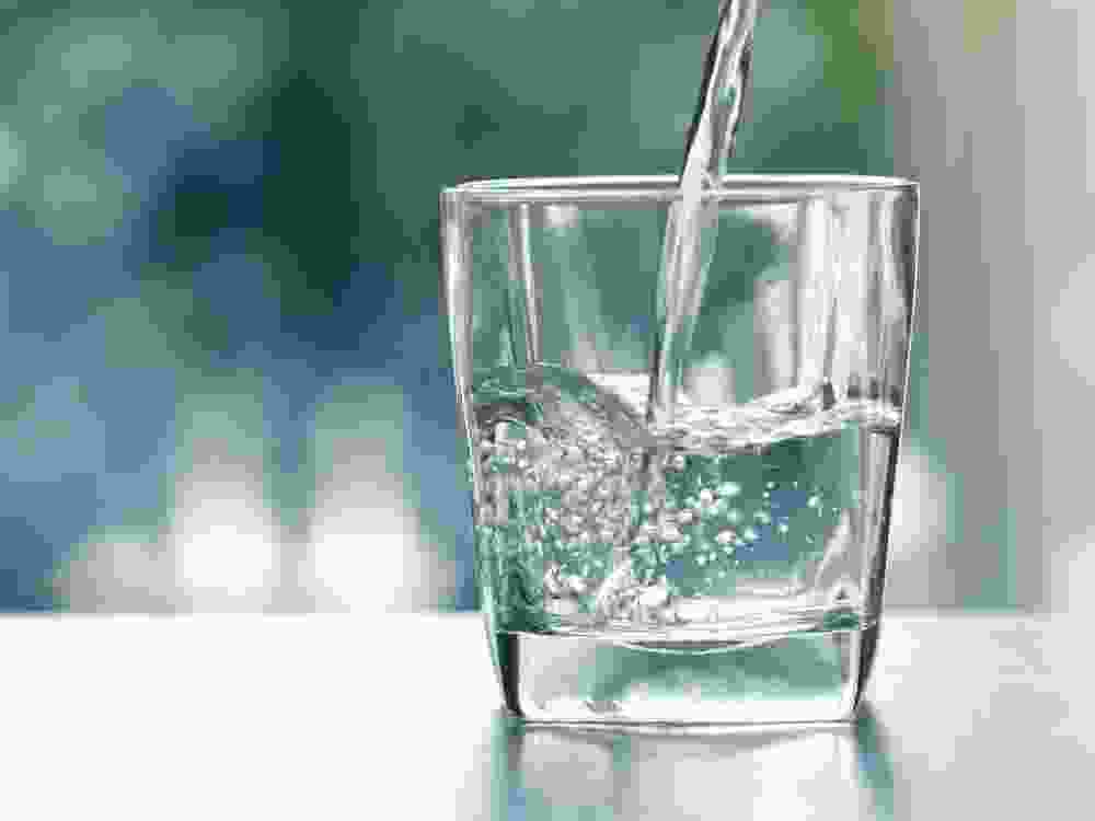 Close up the pouring purified fresh drink water from the bottle on table in living room