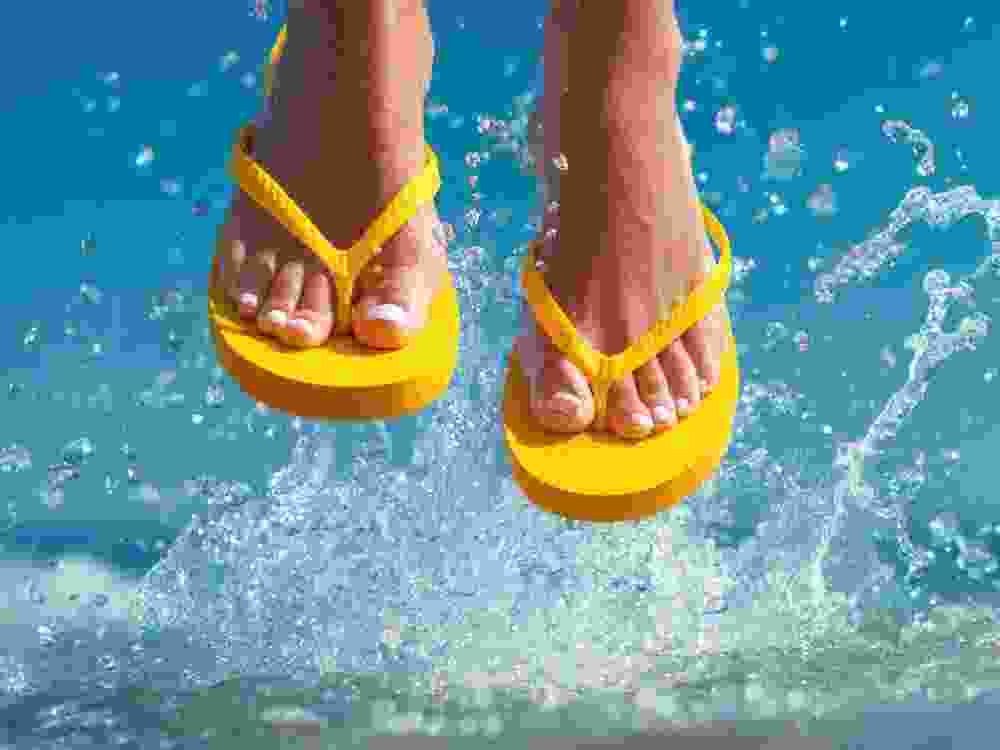 Legs wearing bright yellow flip-flops suspended over ocean waves