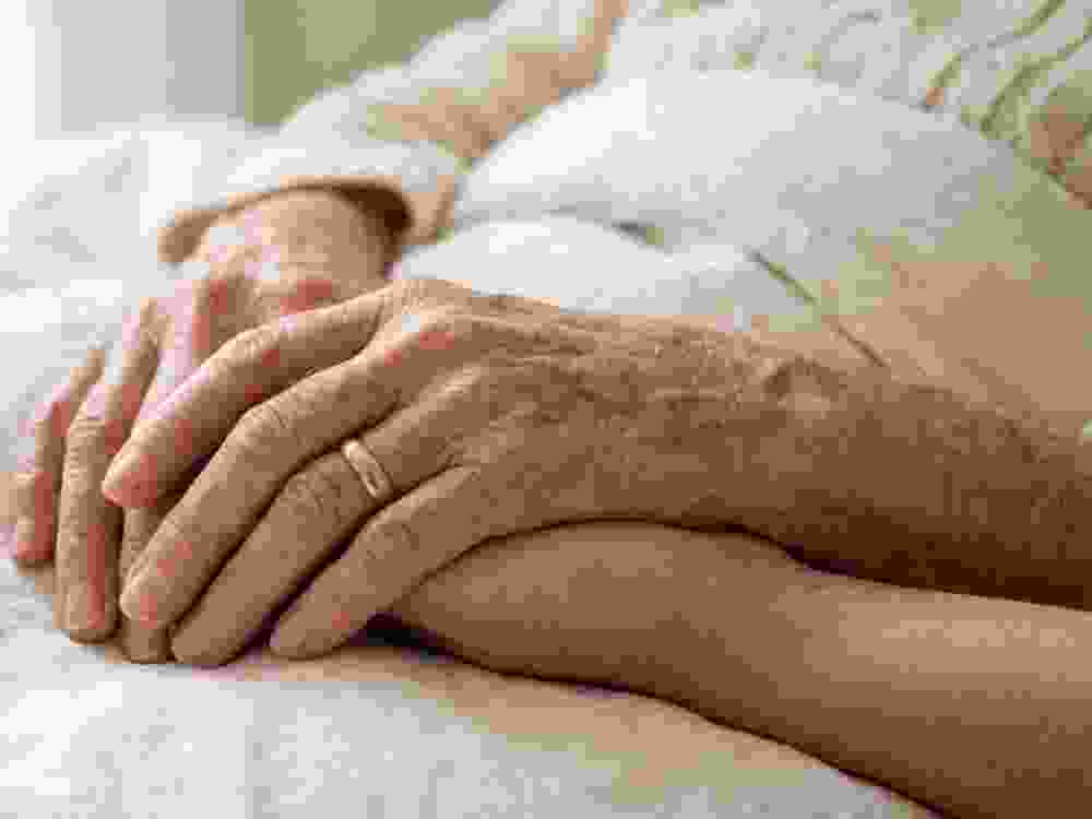 Elderly couple holding hands together while resting in a comfortable bed