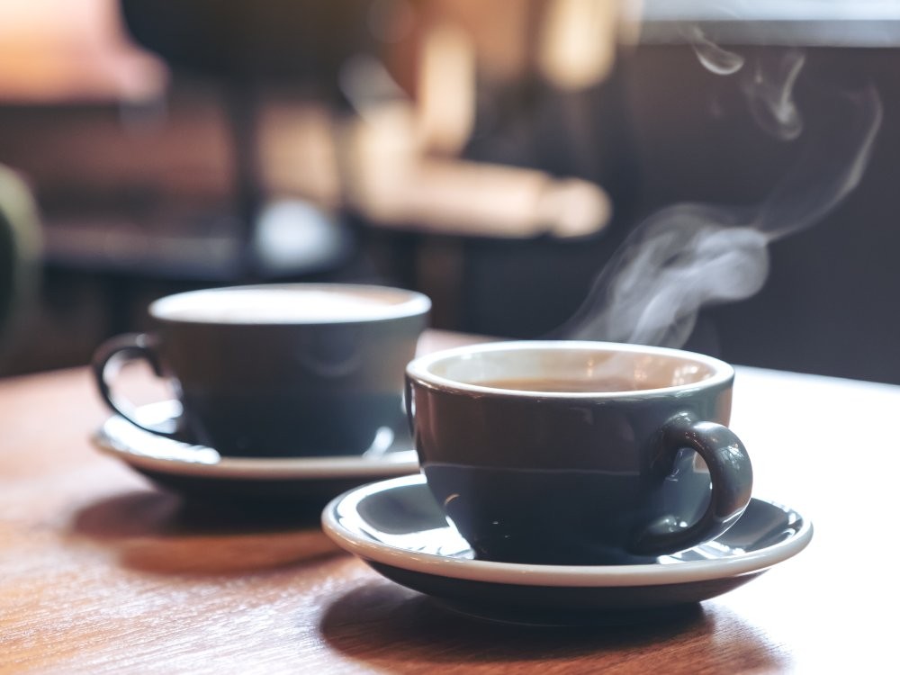 Closeup image of two blue cups of hot latte coffee and Americano coffee on vintage wooden table in cafe