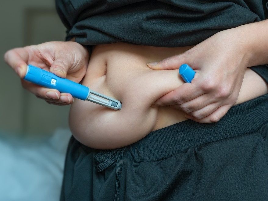 Close-up of a woman injecting a GLP-1 pen into abdominal skin.