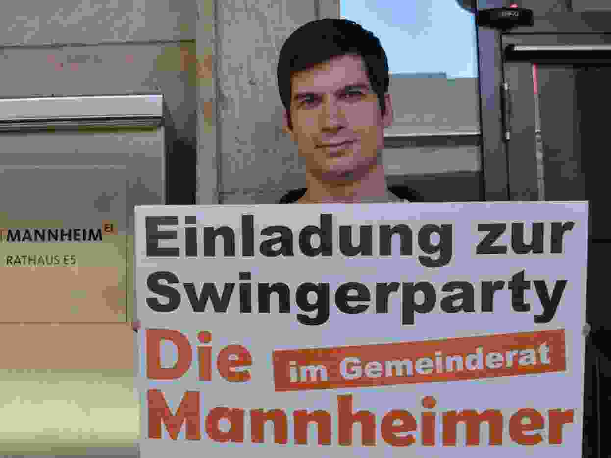 City councillor Julien Ferrat holds sign inviting the citizens of Mannheim to a political swinger party.