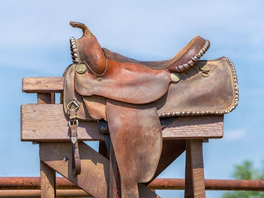 A leather horse saddle displayed on a stand against a blue sky