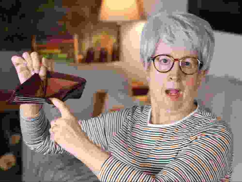A senior woman holds an empty wallet.