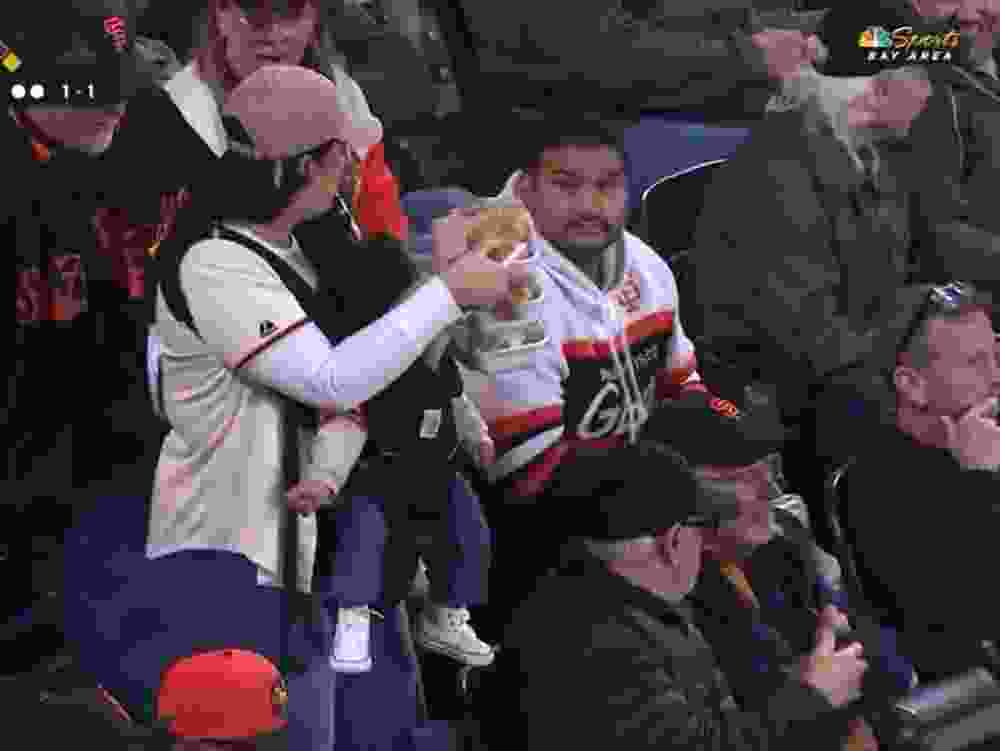 A mother returns to her seat while holding a baby and food during a San Francisco Giants game.