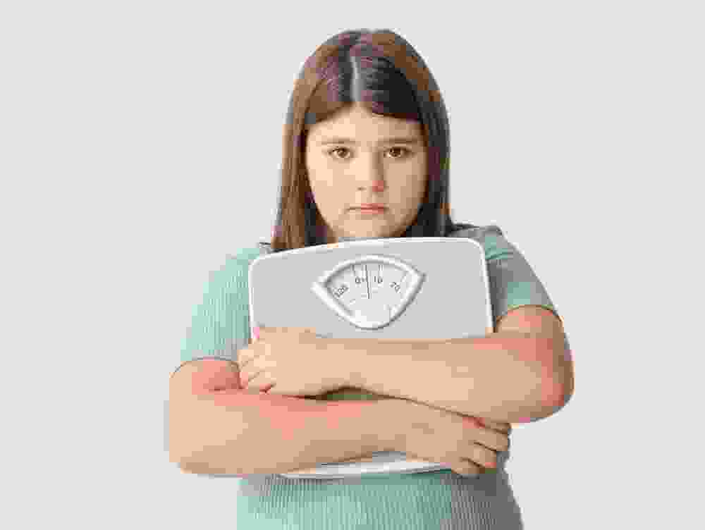 A sad overweight girl holds measuring scales.