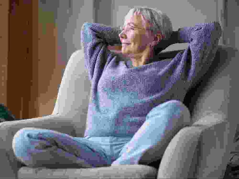 An older woman rests on on a comfortable chair.