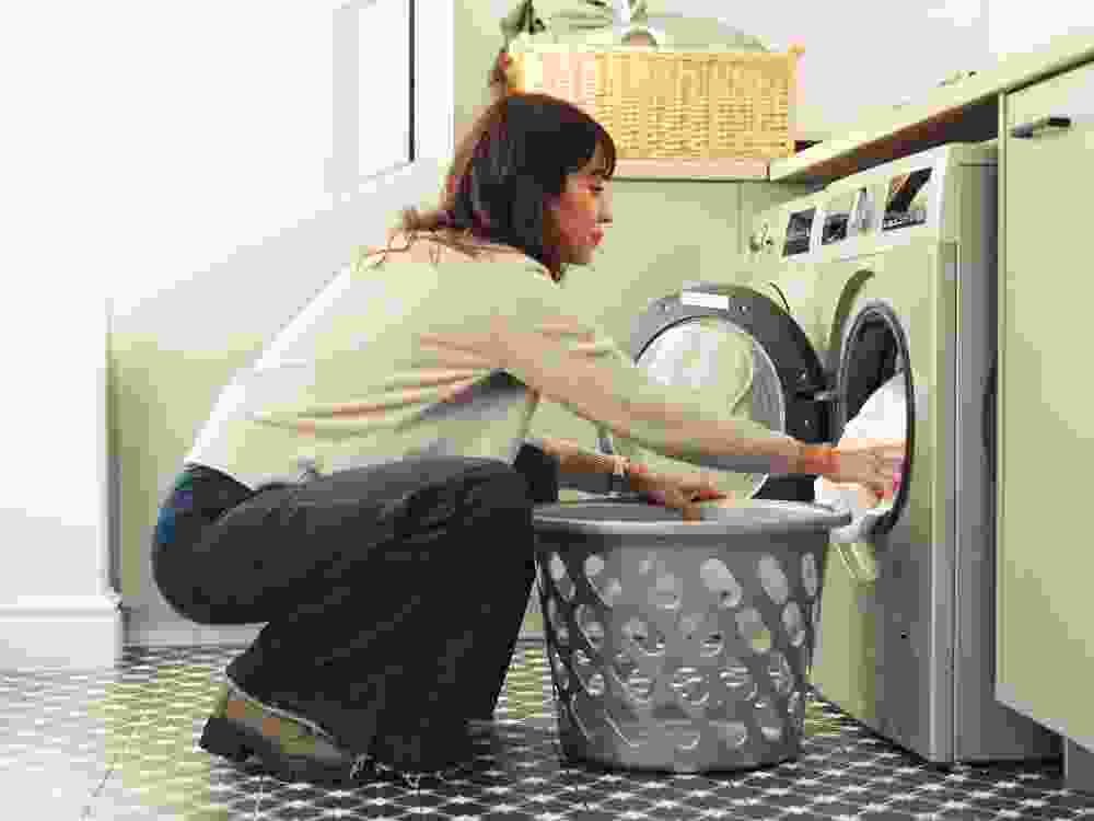 Woman, clothes and washing machine for cleaning in home with basket, fabric and routine for hygiene. Person, container and appliance with laundry, linen or chores with housekeeping at apartment