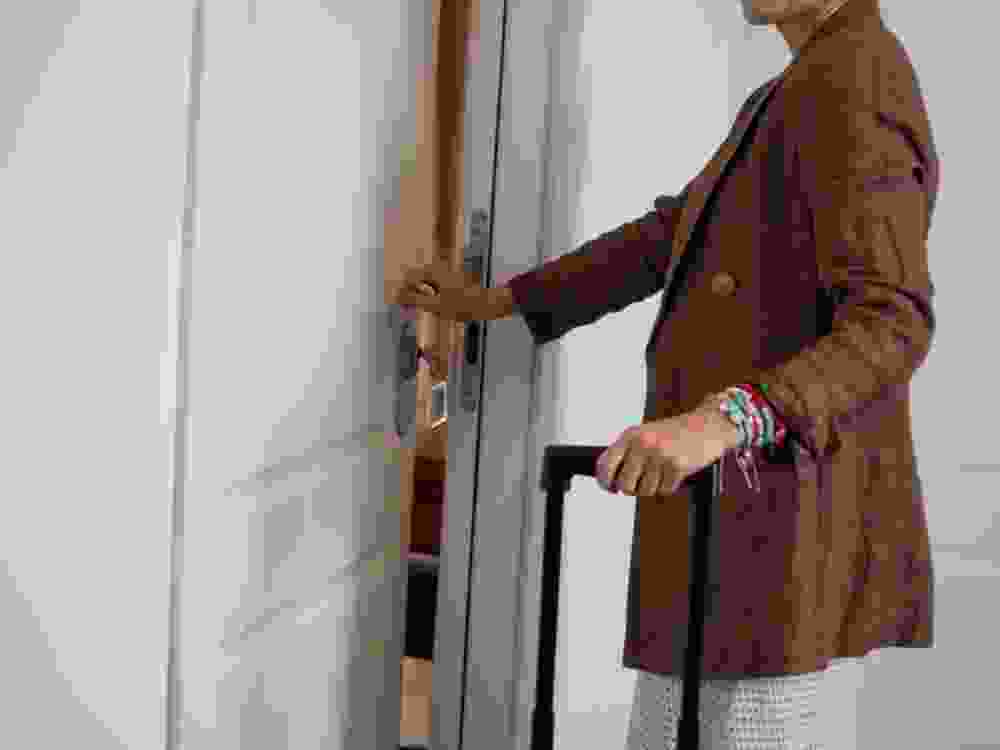Side back view of a female traveler with a blue suitcase reaching for the door handle outside room 305.