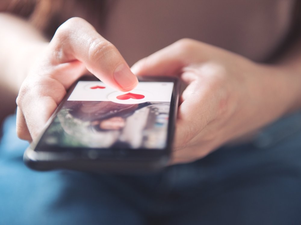 Finger of woman pushing heart icon on screen in mobile smartphone application. Online dating app, valentine's day concept.