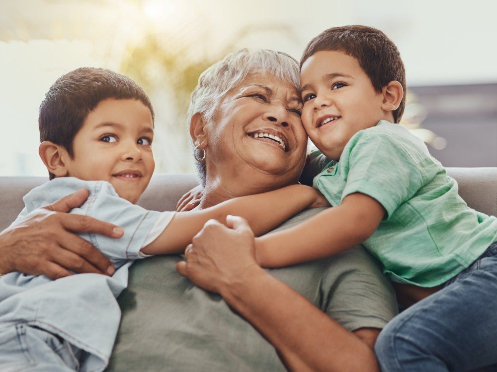 Children, hug and grandmother on a sofa, happy and smile, love and laugh while bonding on their home visit. Kids, grandchildren and boy embrace grandma on a couch, relax and hugging in a living room