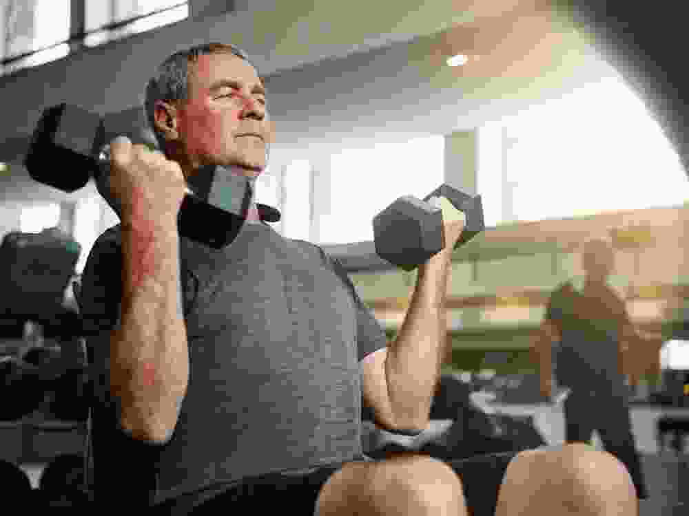 Fitness, gym and senior man with dumbbells for weightlifting, challenge or cardio workout, training or bodybuilding. Biceps, arms and elderly person with hand weight for strength, mindset or exercise