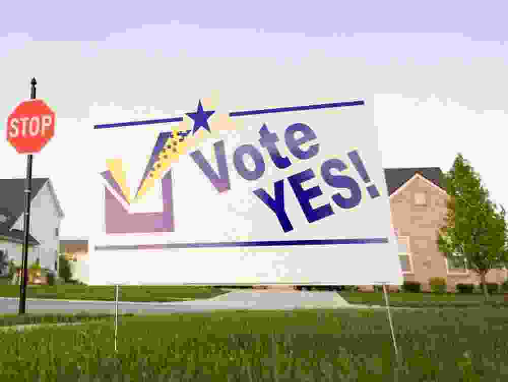 Image of a lawn sign in a neighbourhood reading Vote Yes